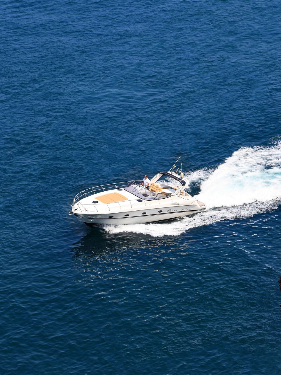 A white motorboat cruises through deep blue water, leaving a bright white wake behind it.