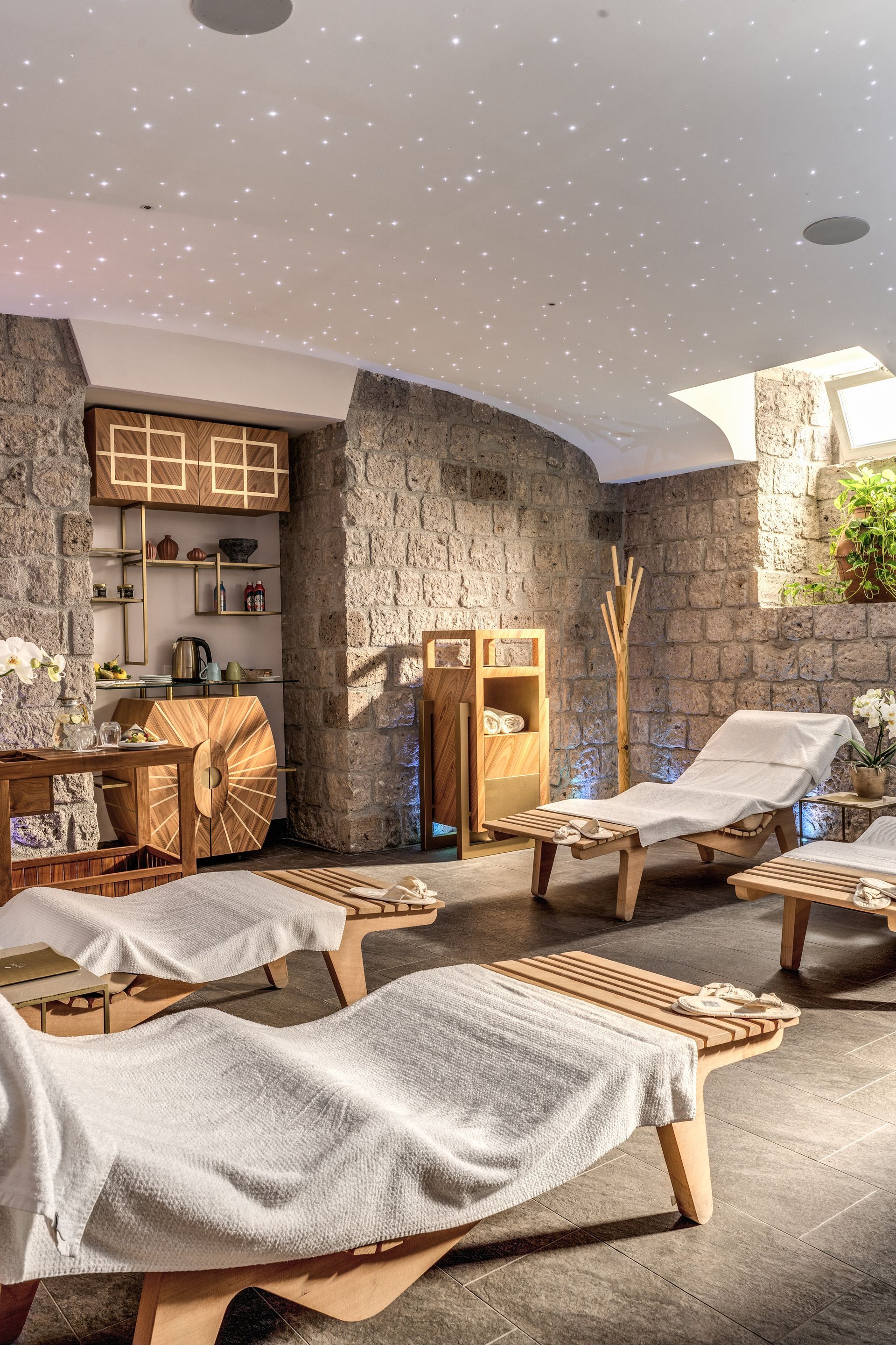 A stone-walled spa relaxation room with wooden lounge chairs, soft white towels, and a starlit ceiling.