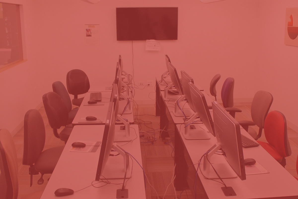 Computer lab with long tables, chairs, and monitors; a TV on the wall.