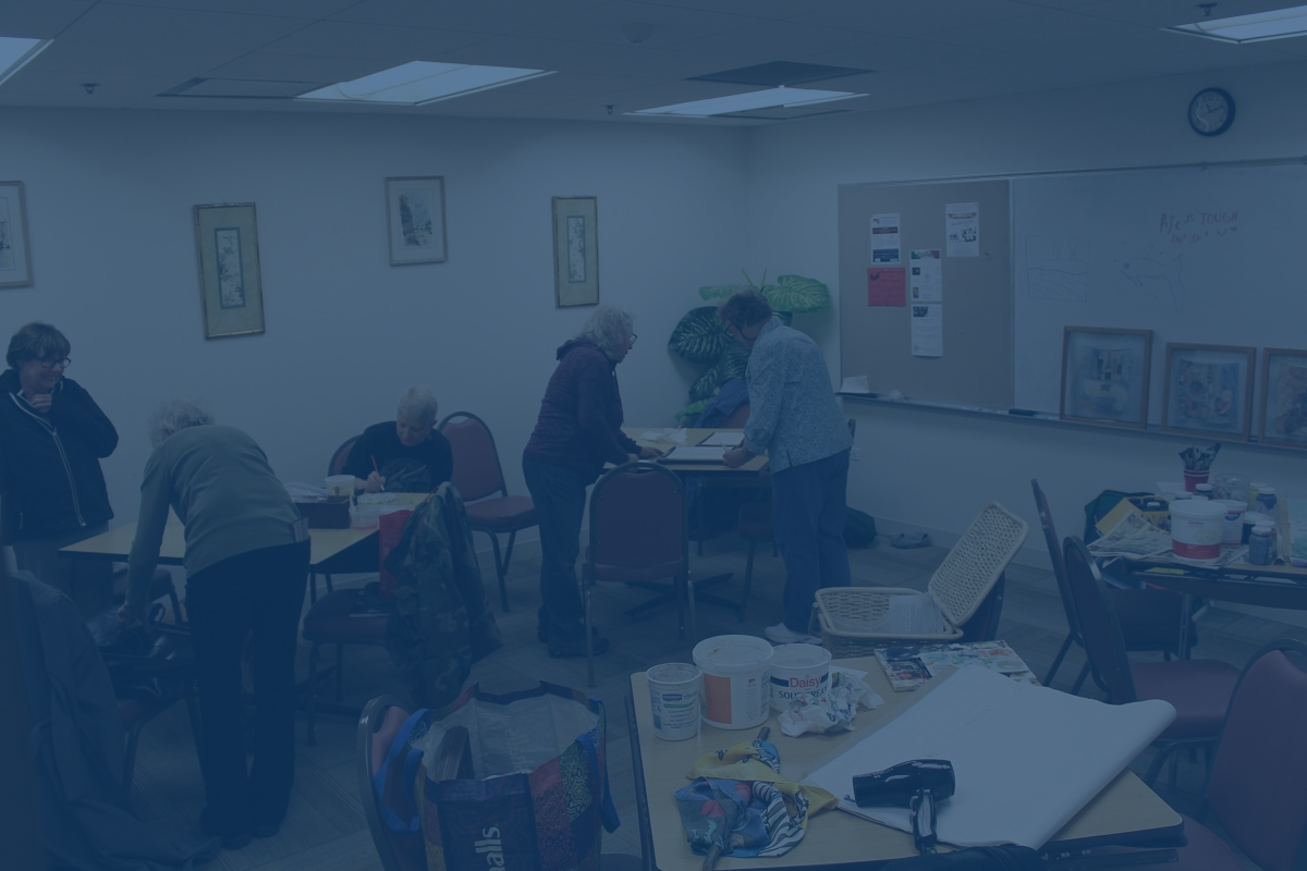 People in a brightly lit room working on art projects at tables, with paintings on the walls.