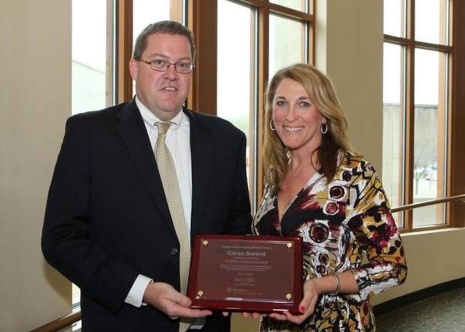 Man in suit presents woman with award plaque in a building with large windows.