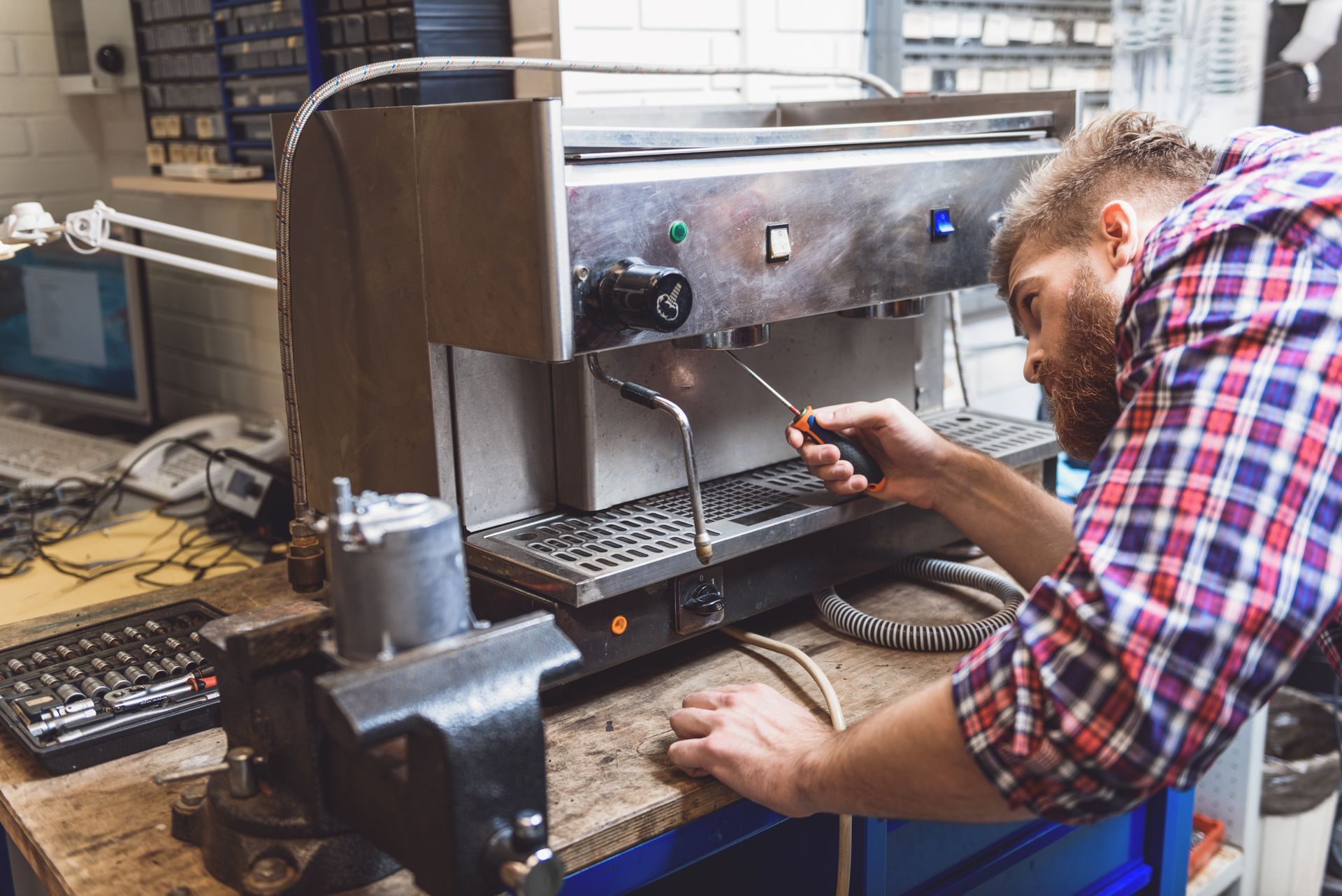 Technician repairing a computer inside a workshop, using a screwdriver at a cluttered workbench