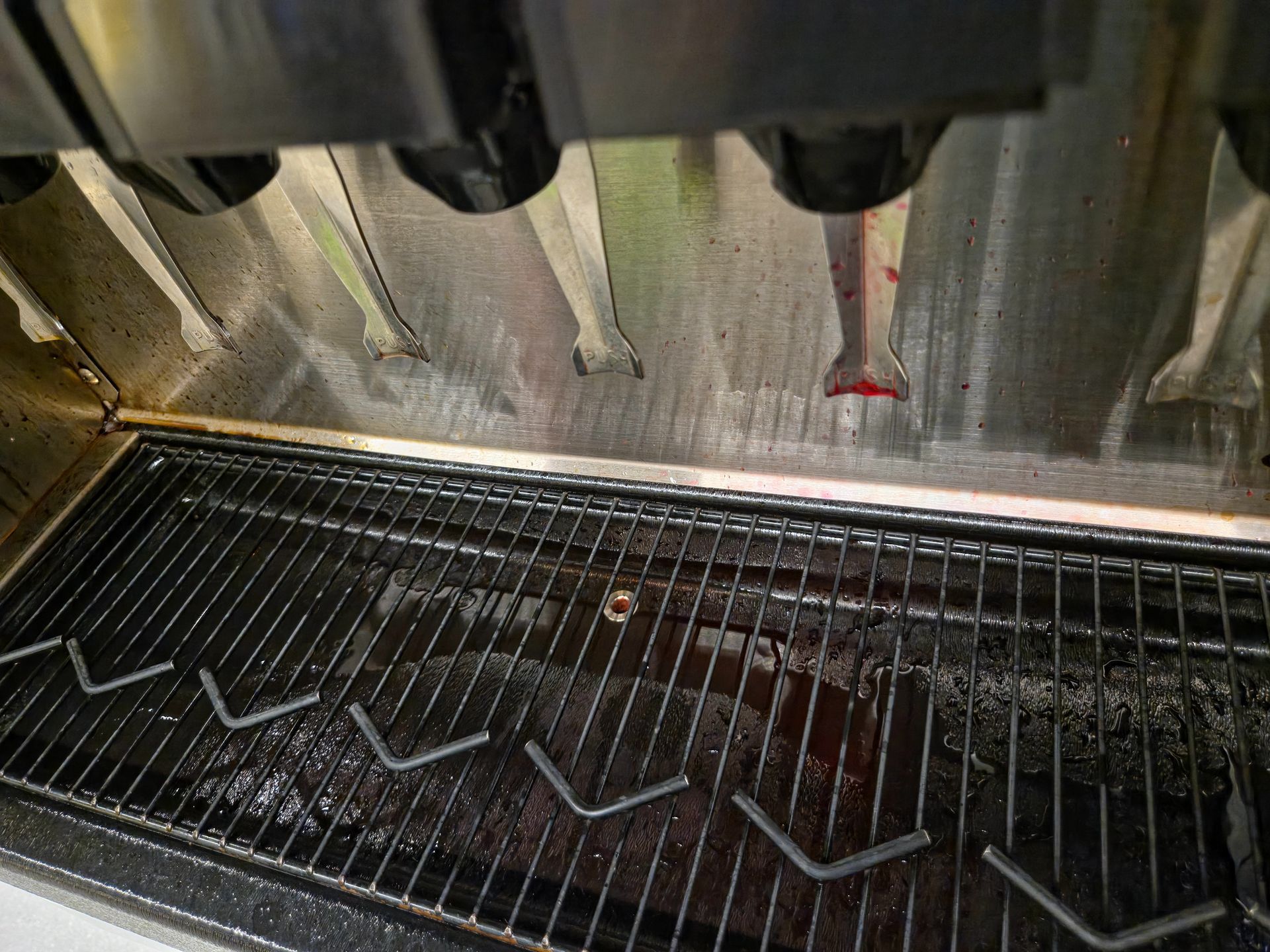 Inside a commercial oven, wire racks hold zigzag strips of dough under metal nozzles.