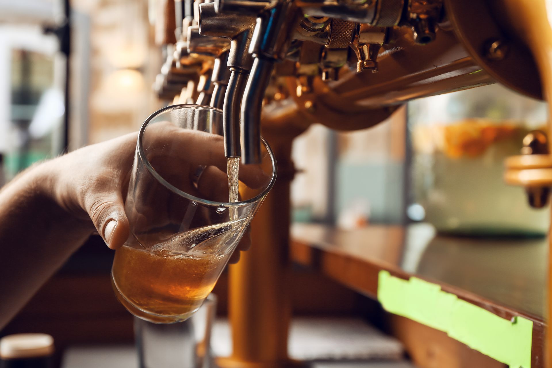 Beer being poured from taps into a glass at a bar, with a hand holding the glass.