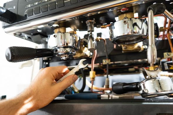 Hand adjusting an espresso machine’s portafilter and controls in a cafe kitchen