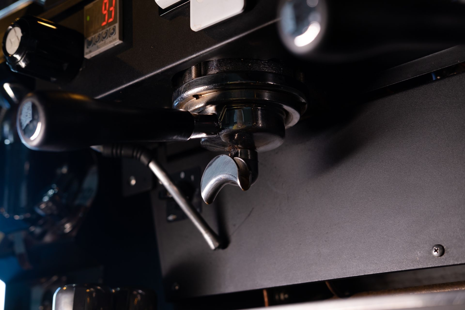 Close-up of a metallic espresso machine portafilter and steam wand in a dimly lit café setting