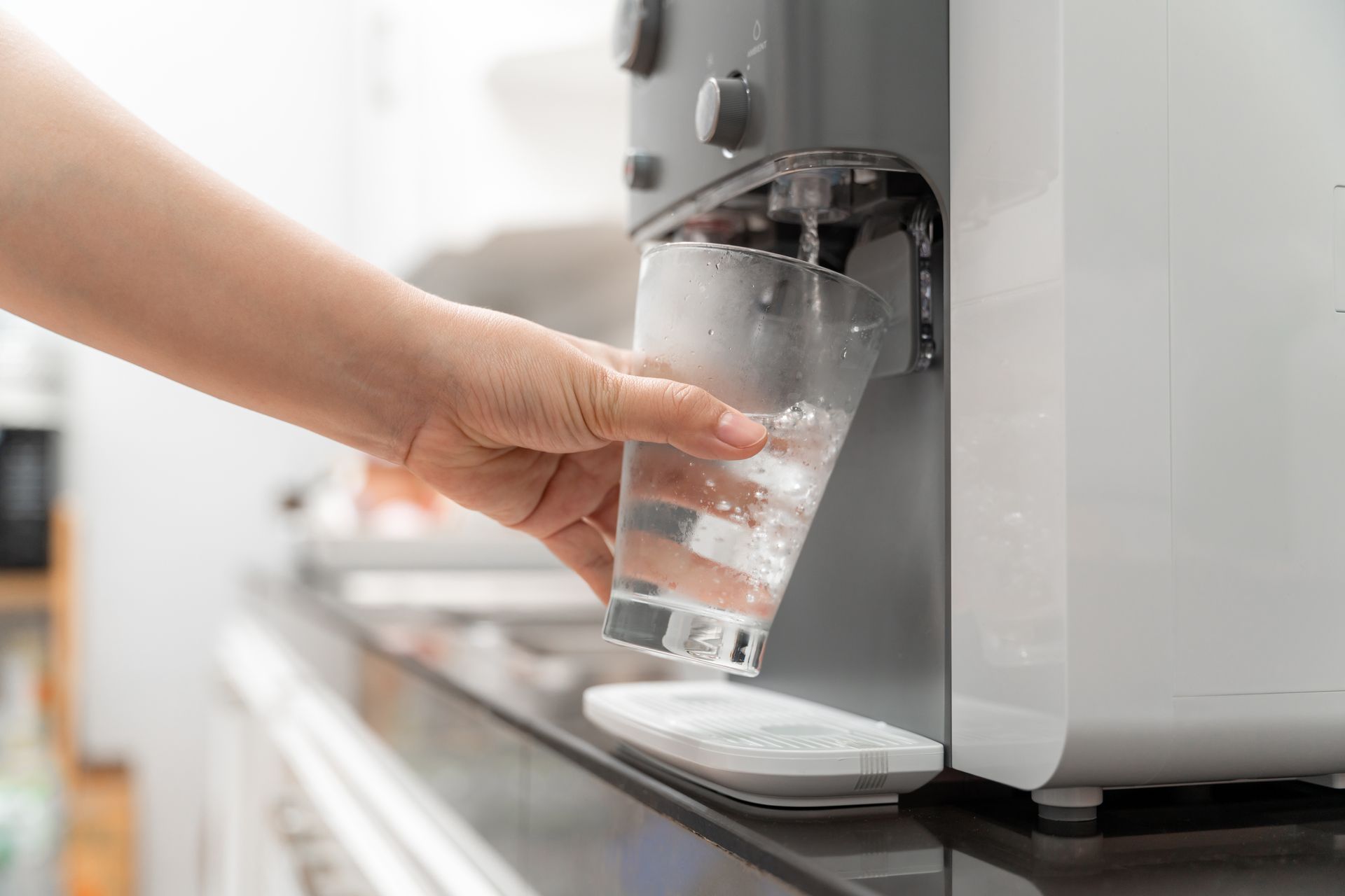 Hand reaching for a glass of water from a countertop dispenser