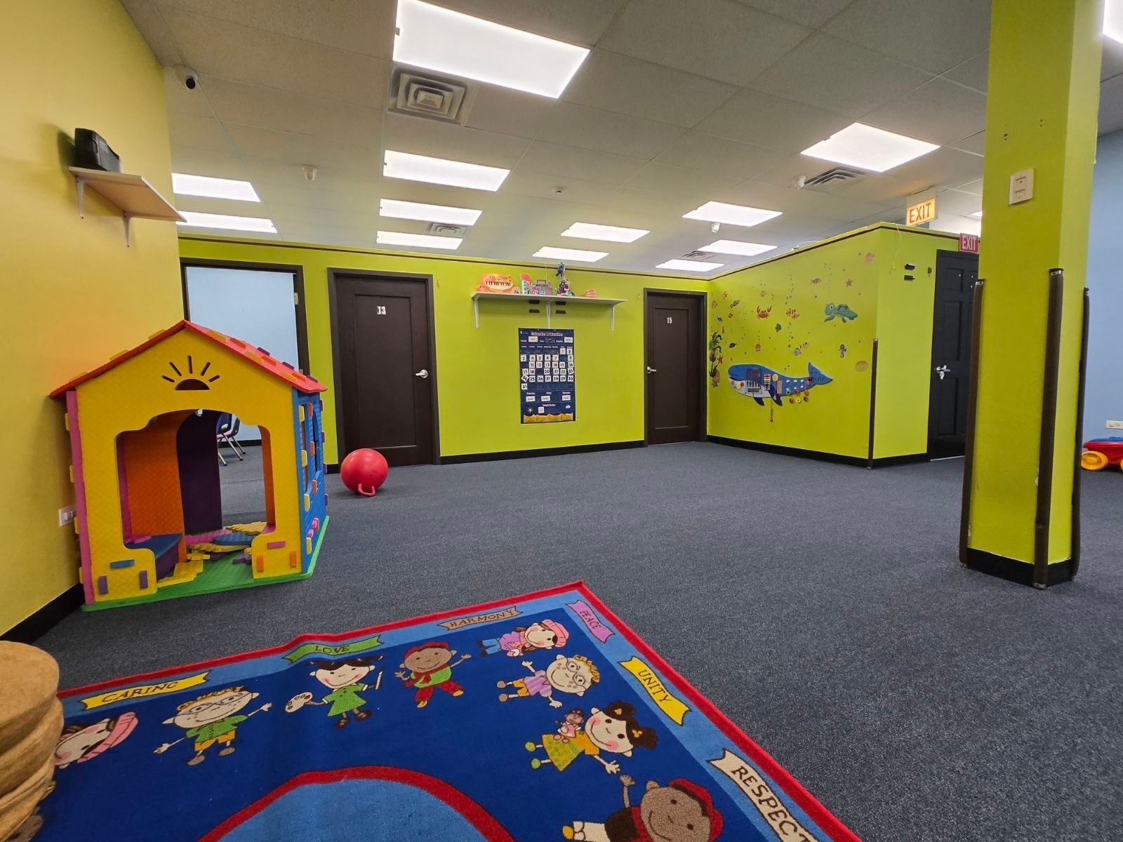 Bright kids’ playroom with yellow walls, blue carpet, toy house, and a red ball.