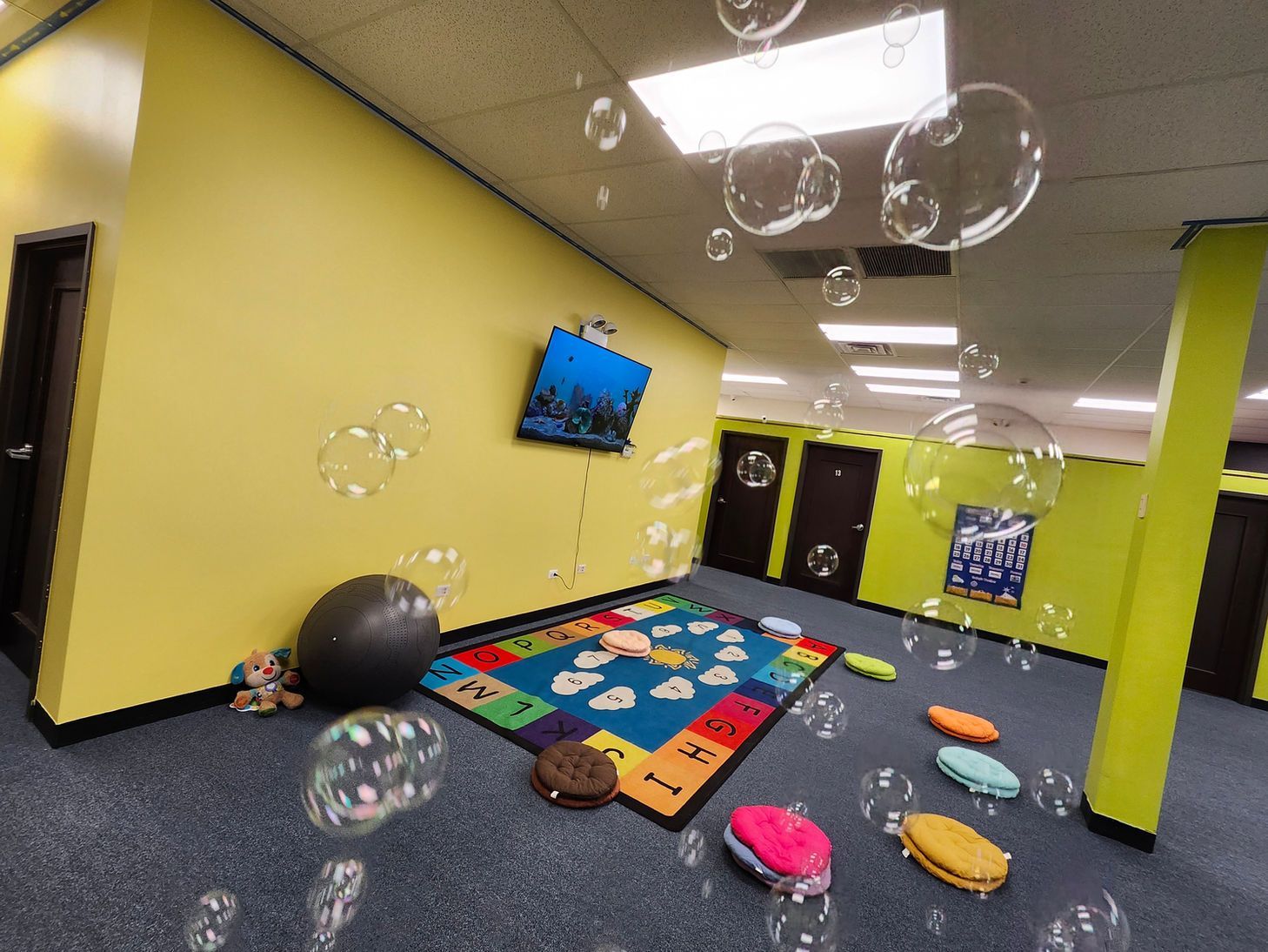 Children’s playroom with colorful mats, balls, wall TV, and hanging bubble lights on yellow walls