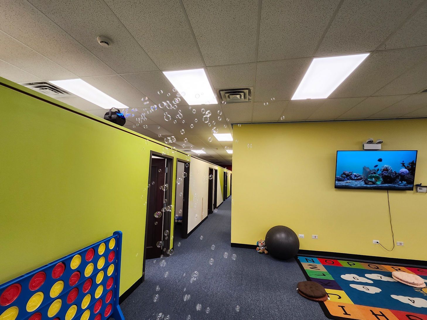 Indoor playroom with lime walls, blue carpet, a wall-mounted TV, and colorful play mats.