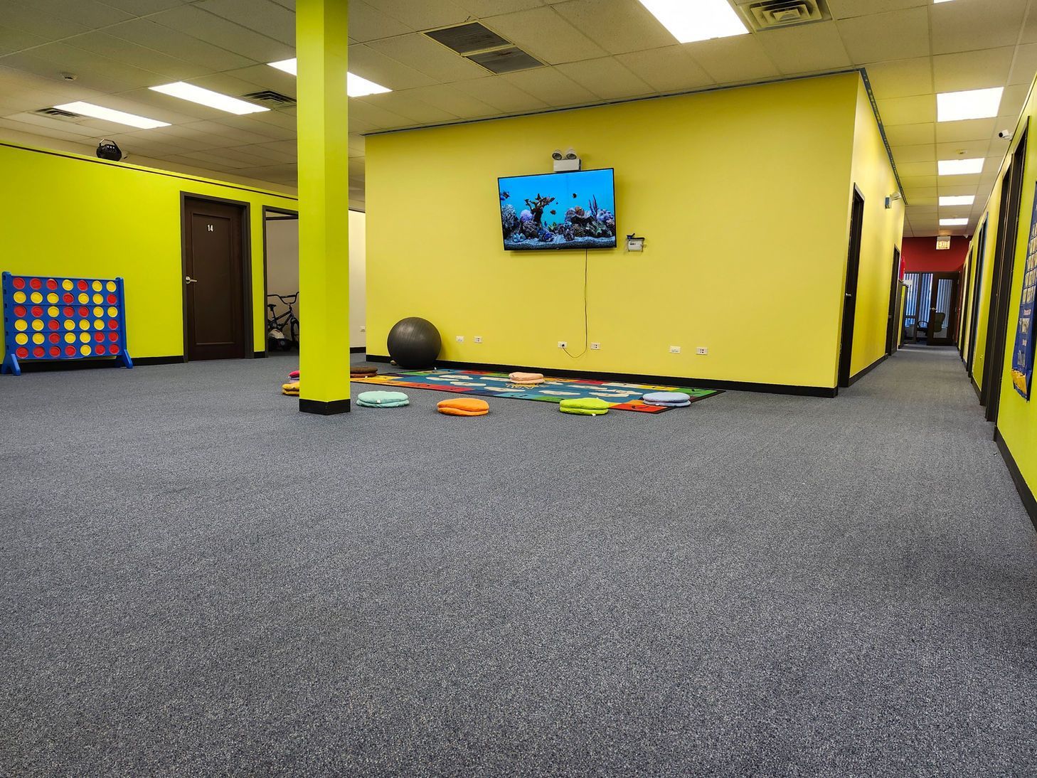 Spacious indoor playroom with gray carpet, yellow walls, a TV, and colorful foam toys on the floor