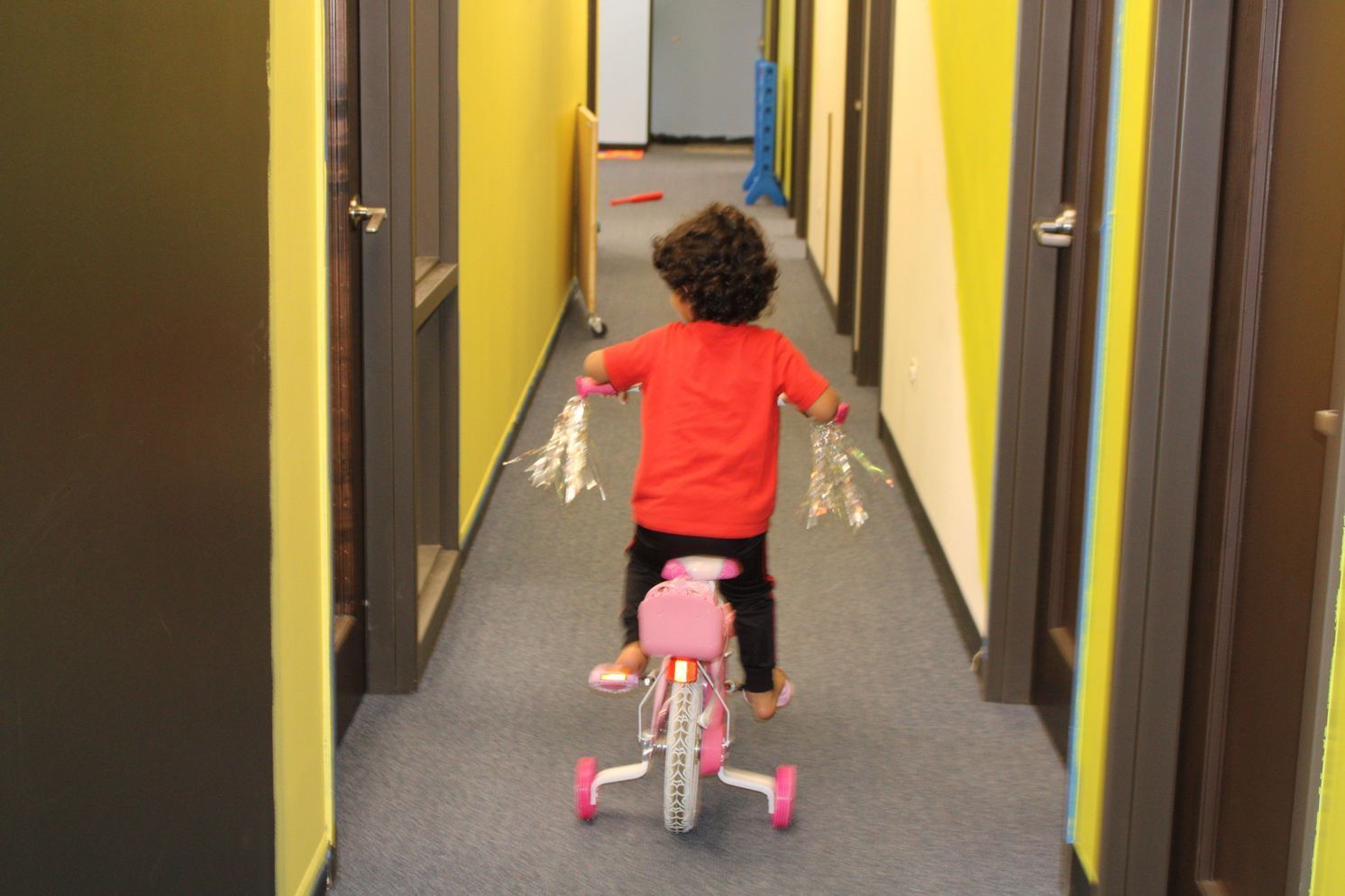 Child riding a pink tricycle down a hallway with yellow walls