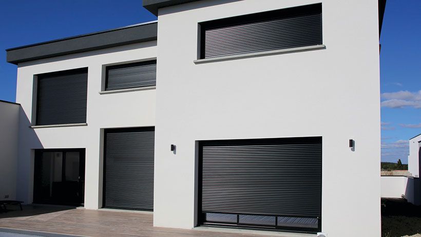 Modern wit huis met zwarte luiken en garagedeur tegen een blauwe lucht.