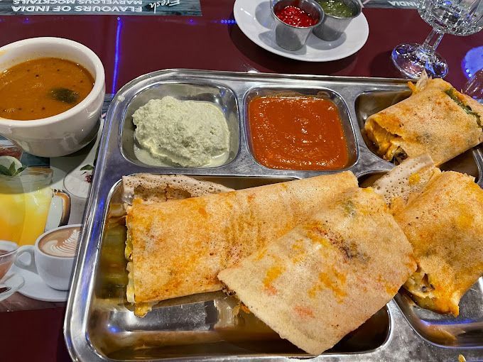 South Indian meal with dosa, chutneys, sambar, and dessert on a metal tray at a table