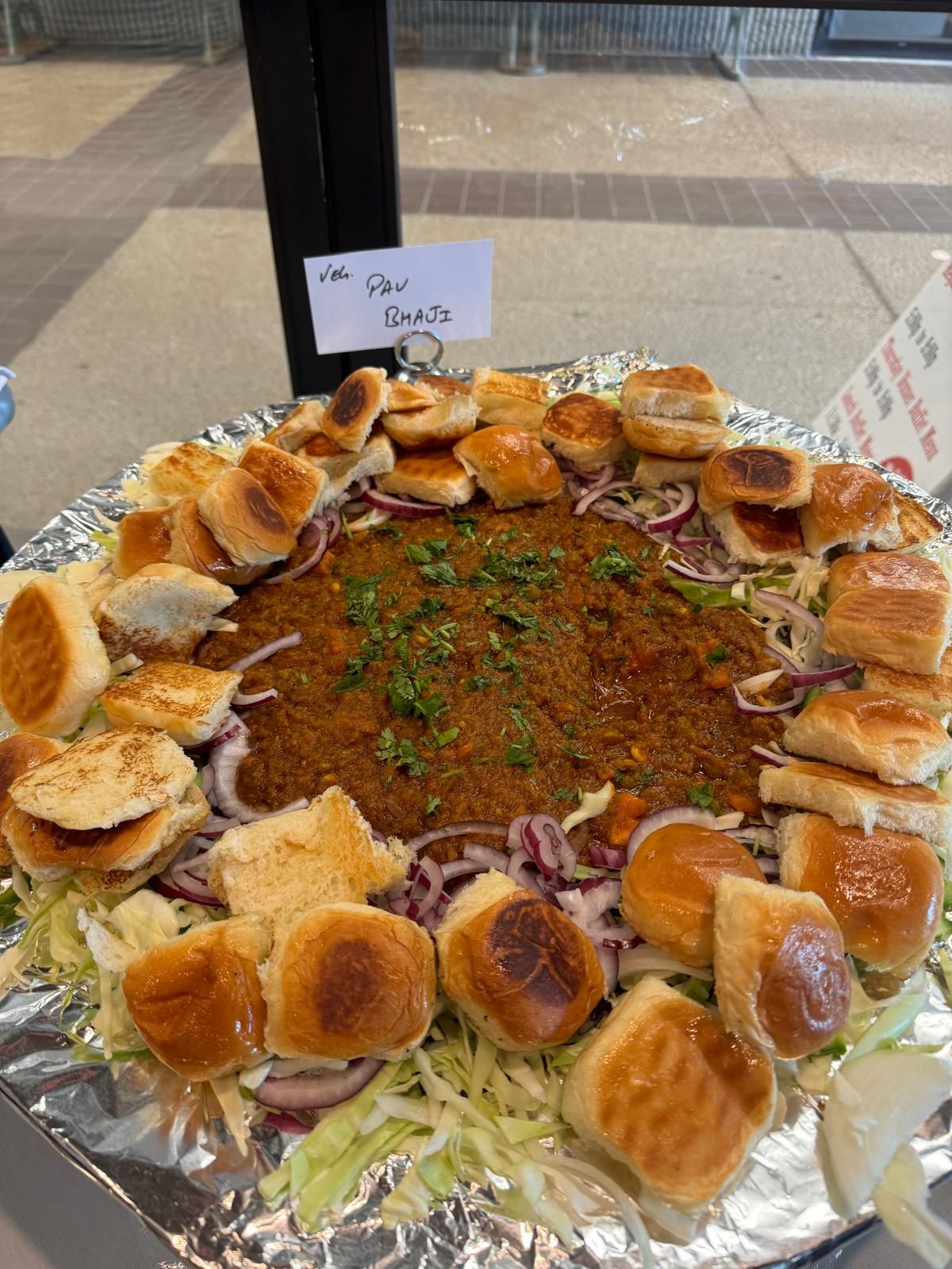 Tray of stuffed buns arranged around a spiced meat dish, served on foil at an outdoor table.