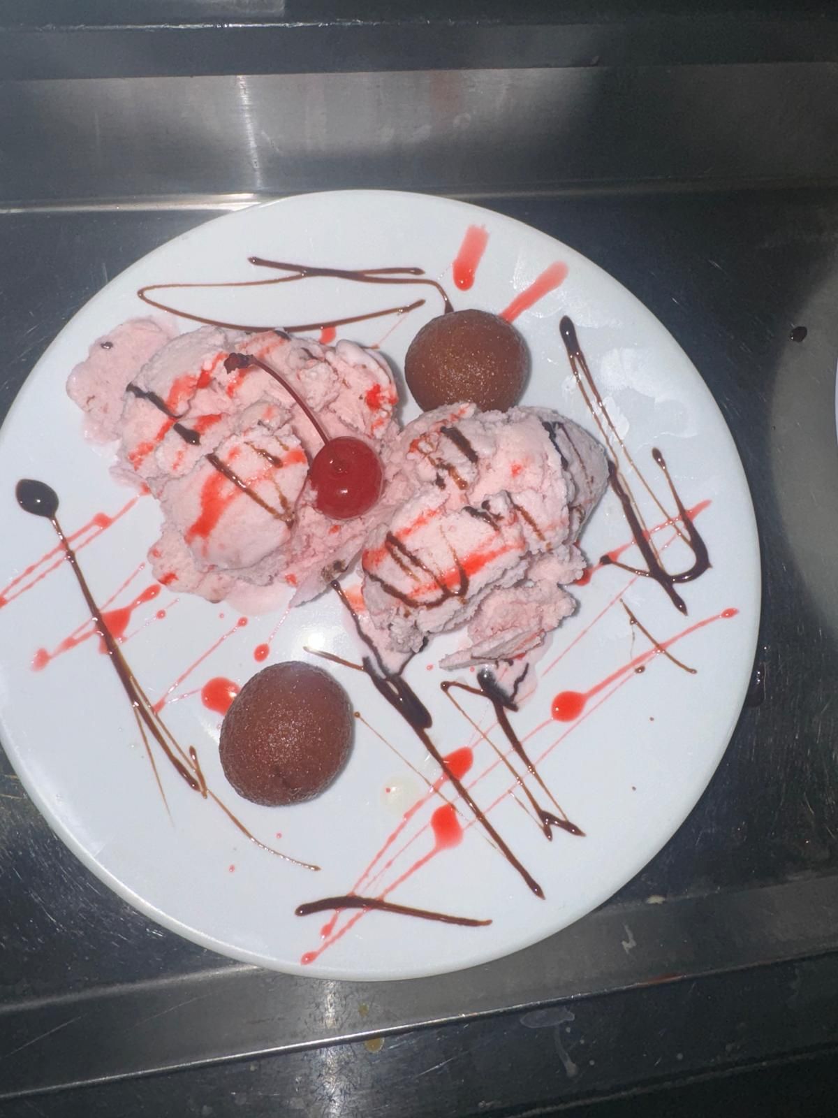 Dessert plate with ice cream, chocolate cookies, and red and chocolate sauce drizzles