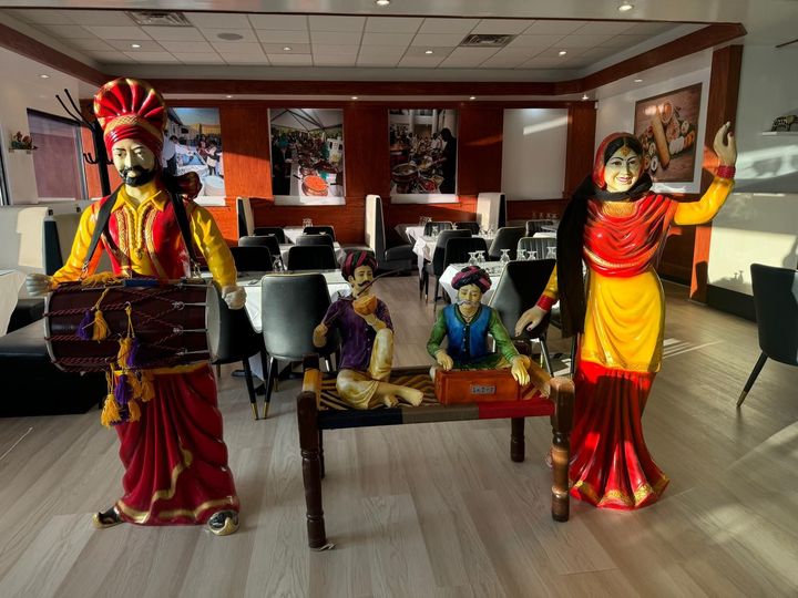 Colorfully dressed dancers posing indoors in a lobby, with one seated and two standing with raised arms.