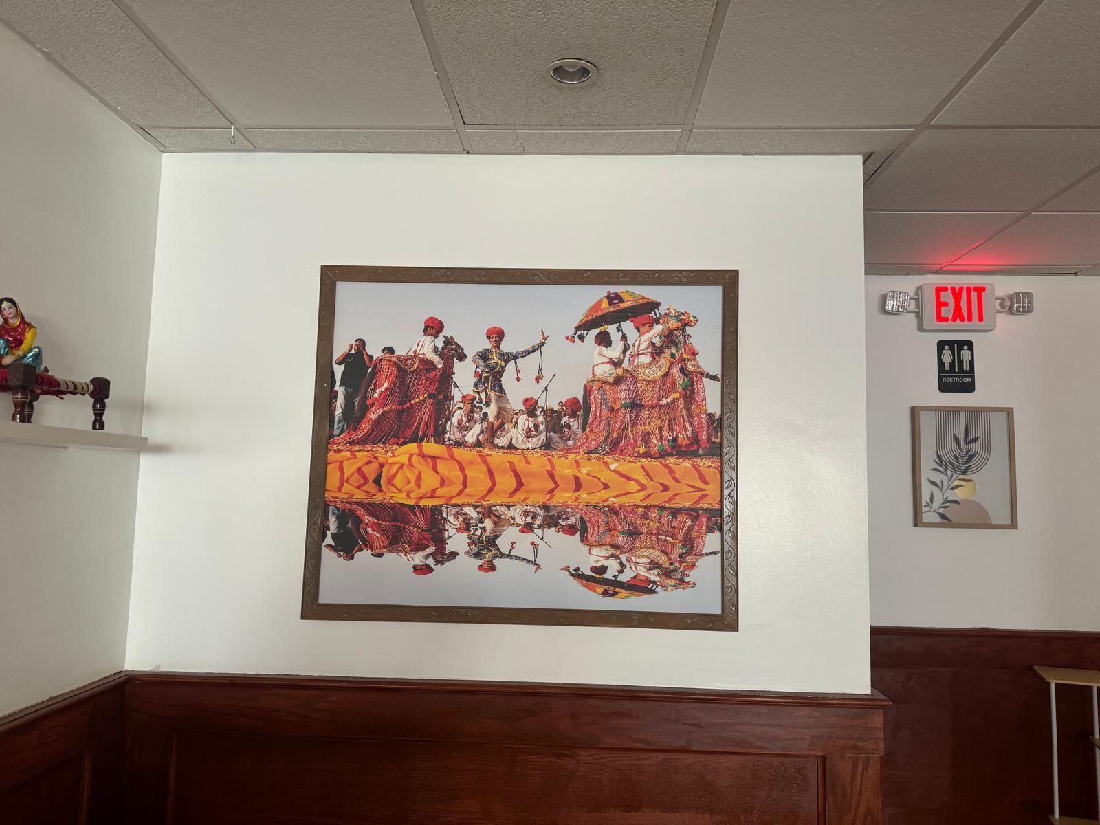 Framed colorful mural on a white wall in a hallway above dark wood paneling and beneath a ceiling light.