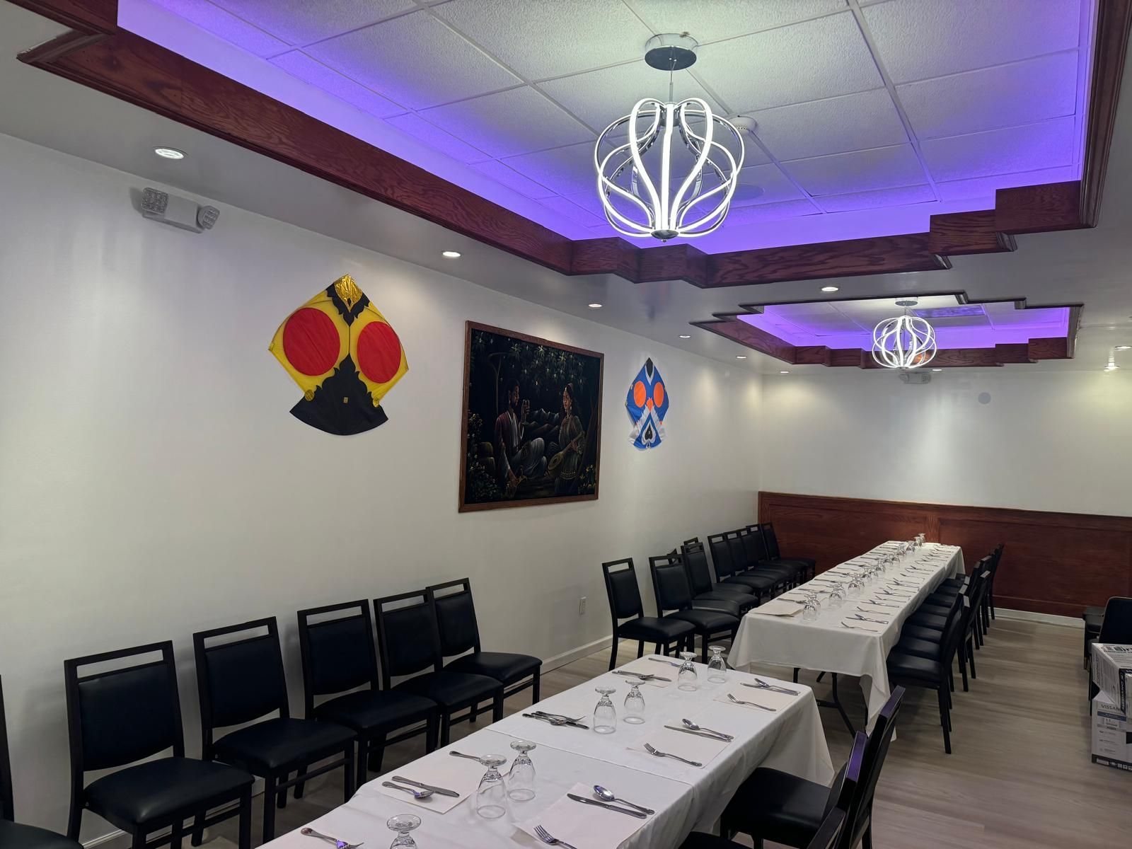 Dining room with long tables, black chairs, and purple ceiling lights in a modern restaurant setup