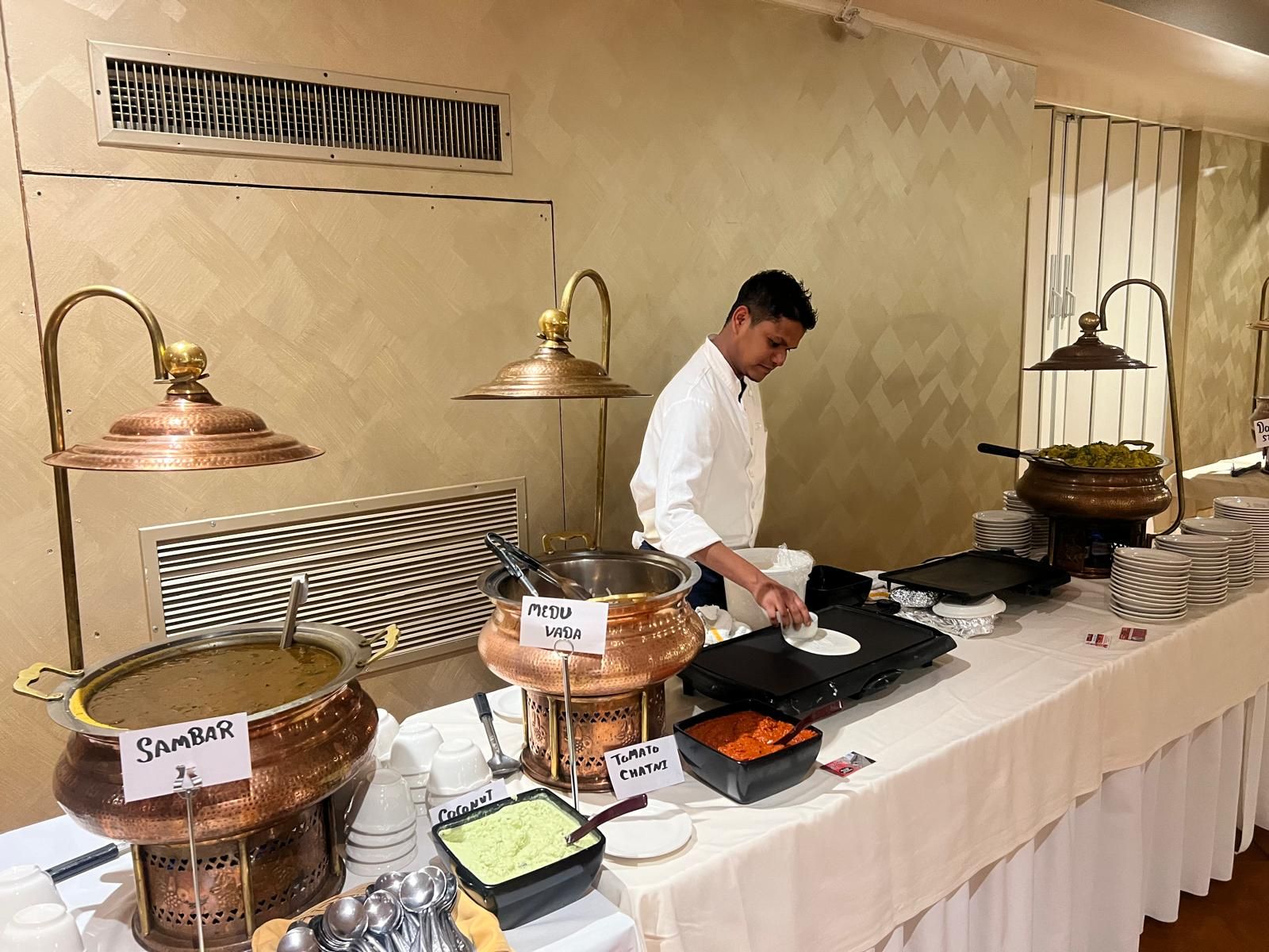 Buffet chef plating food at a catered station with warming trays and covered serving dishes