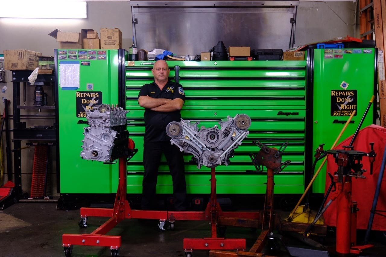 Mechanic standing before a green industrial machine with engine parts on stands in a workshop