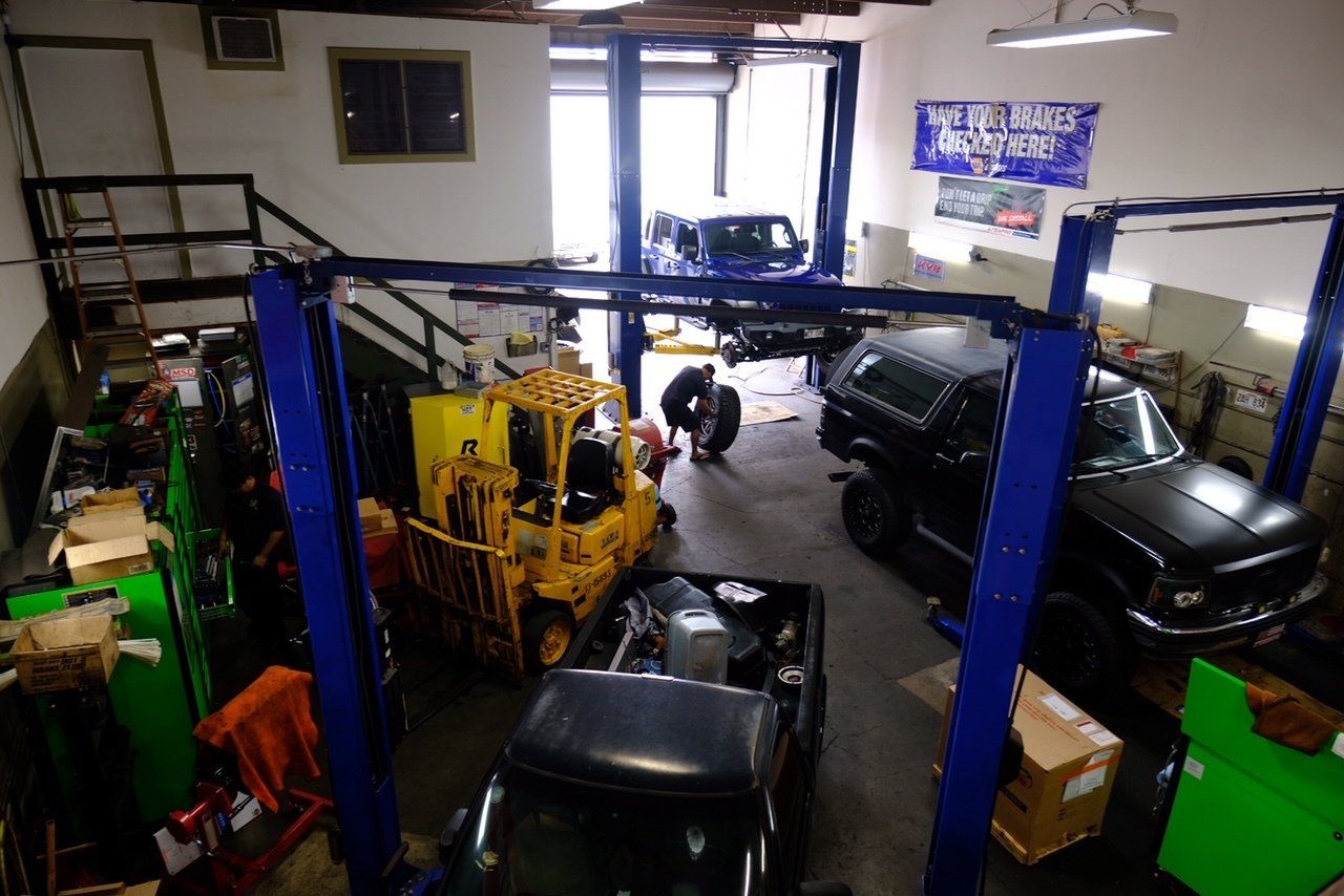 Auto repair shop with several cars, a yellow lift, and a mechanic working in the center.