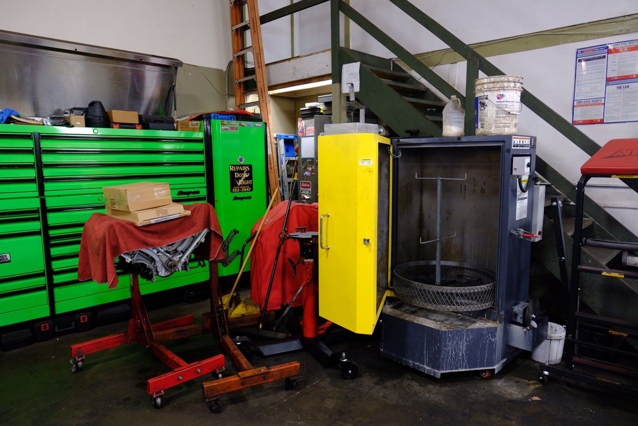 Auto repair shop with green tool cabinets, red floor jacks, and a yellow machine beside a metal tank.