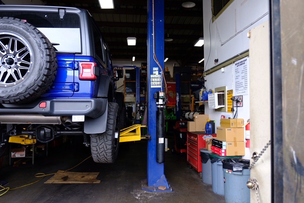 Blue SUV on a lift in an auto repair shop with tools and supplies along the wall