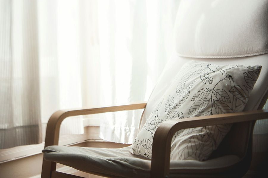 A chair with a pillow on it is sitting in front of a window.