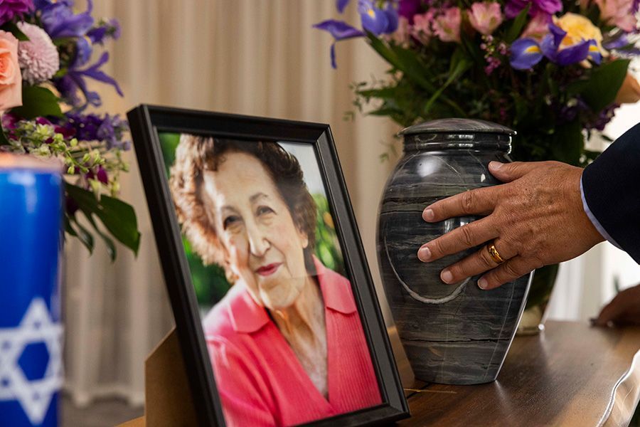 A man is holding an urn in front of a picture of an elderly woman.