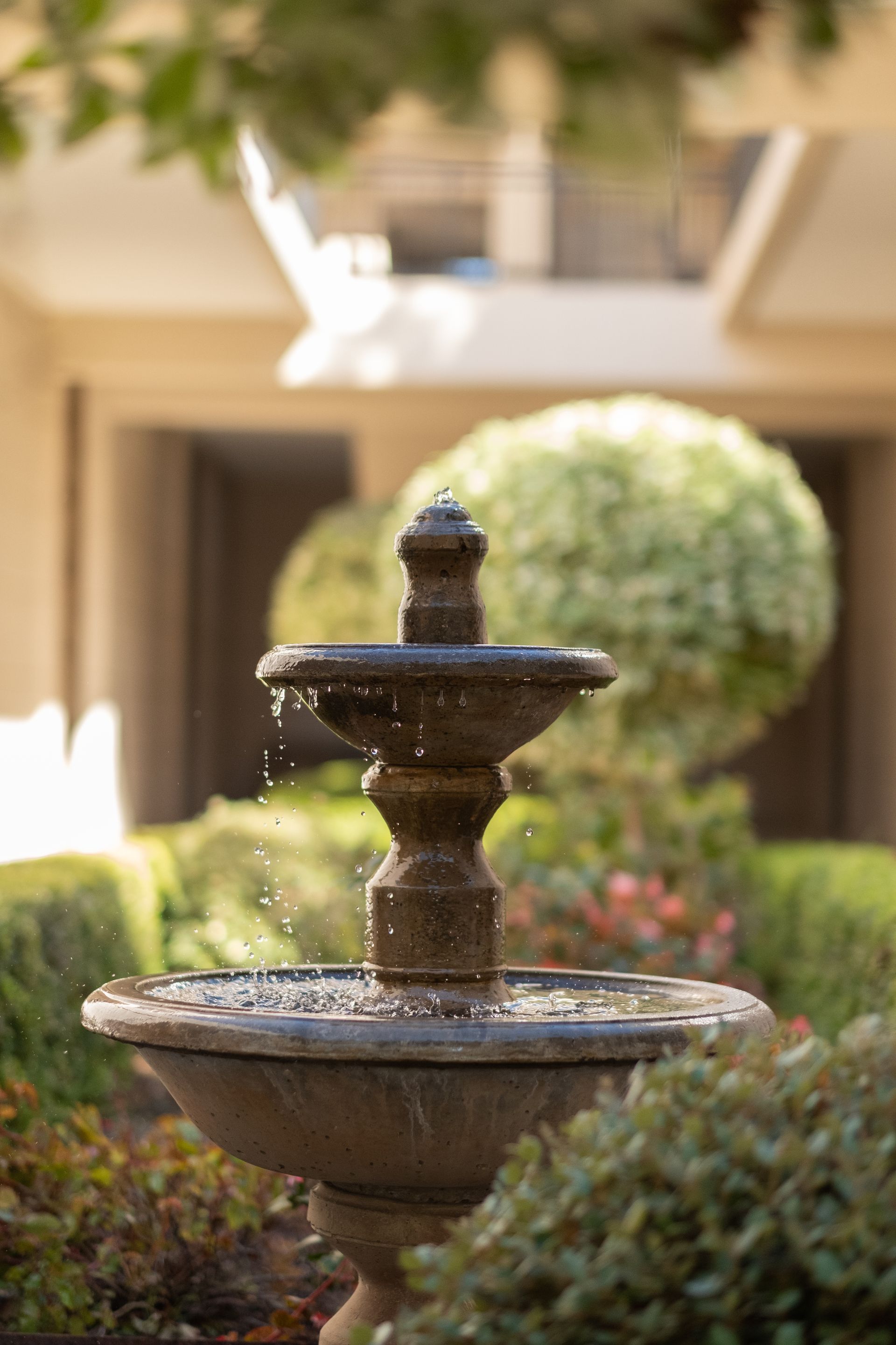 A fountain is in the middle of a garden in front of a building.