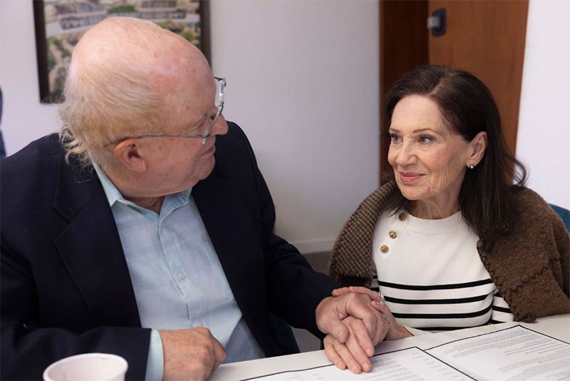 A man and a woman are sitting at a table looking at a book.