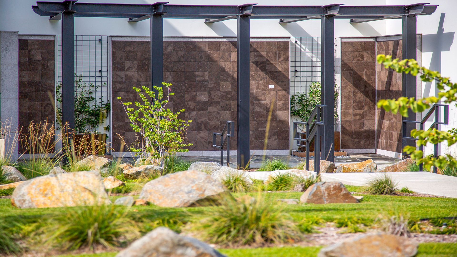 There is a pergola in the middle of a garden in front of a building.