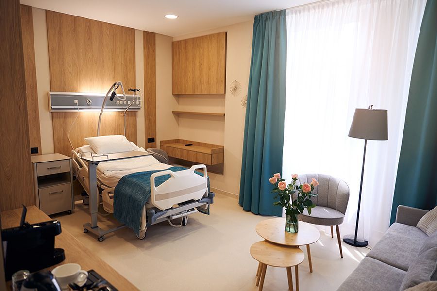 A hospital room with a bed , chairs , tables and curtains.