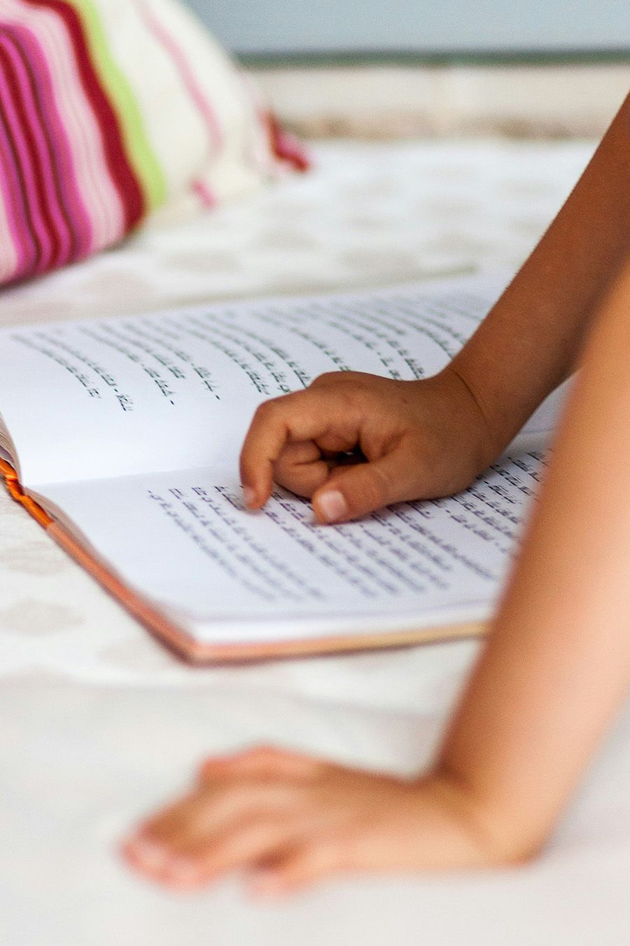 A child is sitting on a bed reading a book