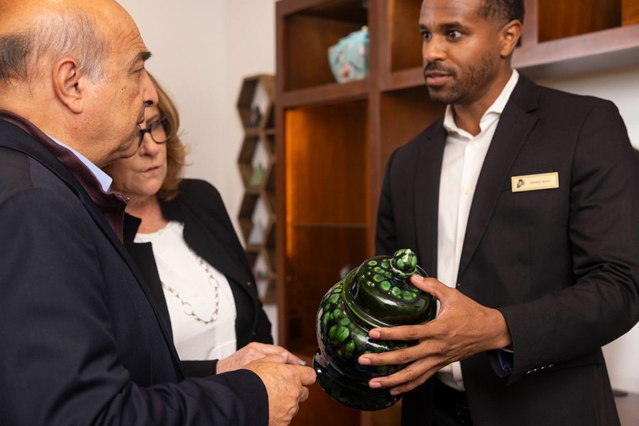 A man in a suit is holding a green vase in front of a group of people.