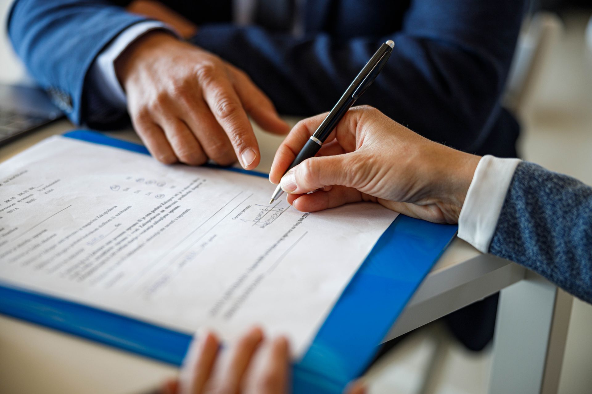 A man and a woman are signing a document with a pen.