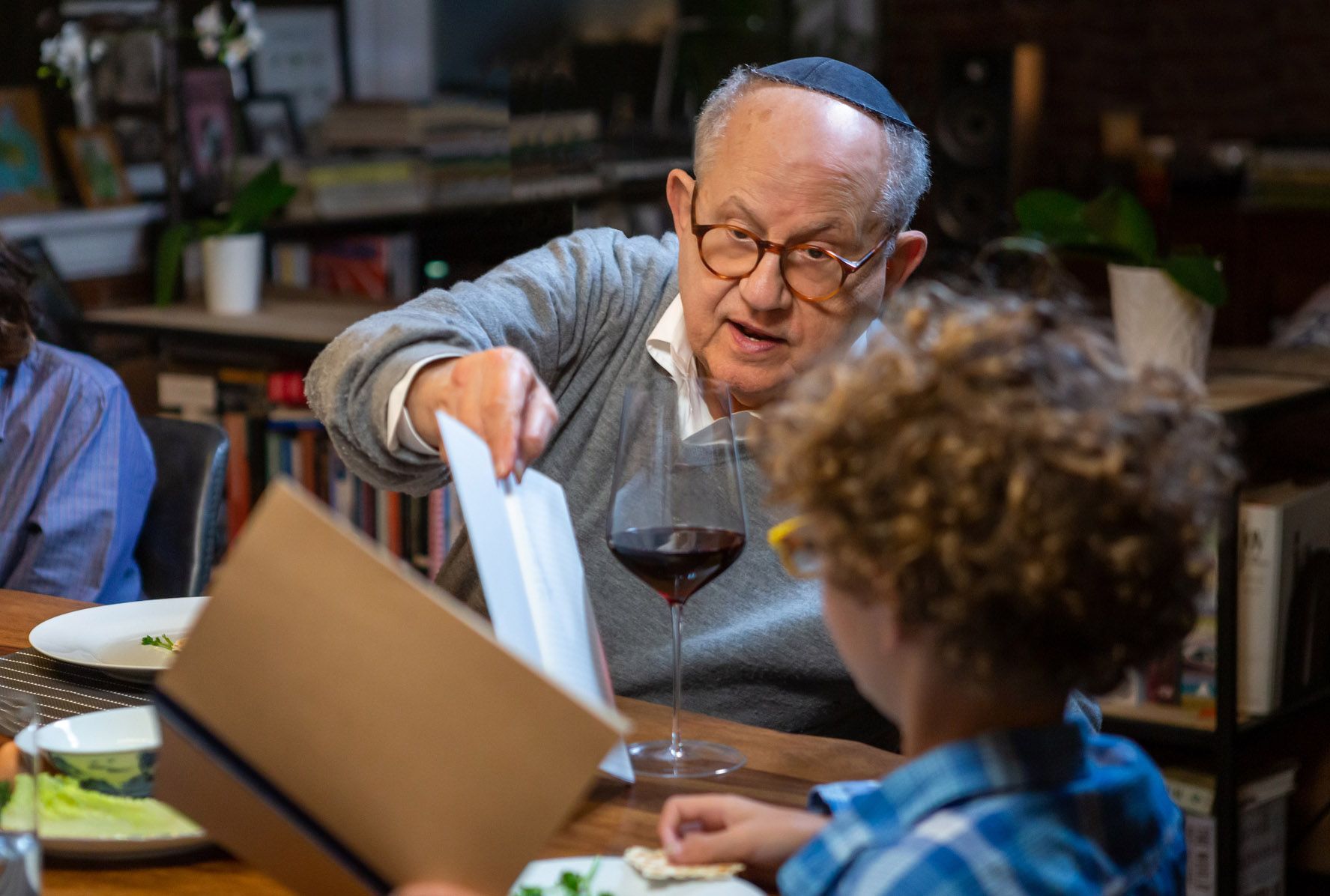 An elderly man is giving a menu to a young boy while sitting at a table.