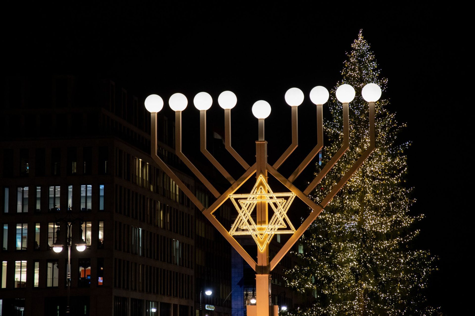 A menorah is lit up in front of a christmas tree.