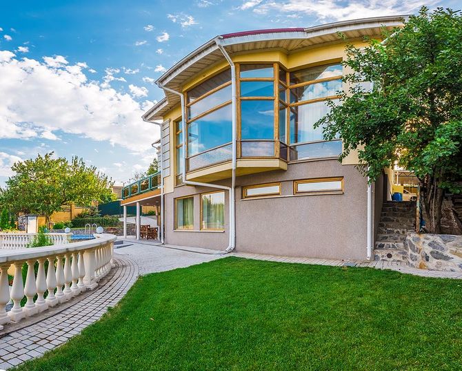 Modern house with large windows, green lawn, stone balustrade, and a blue sky backyard view