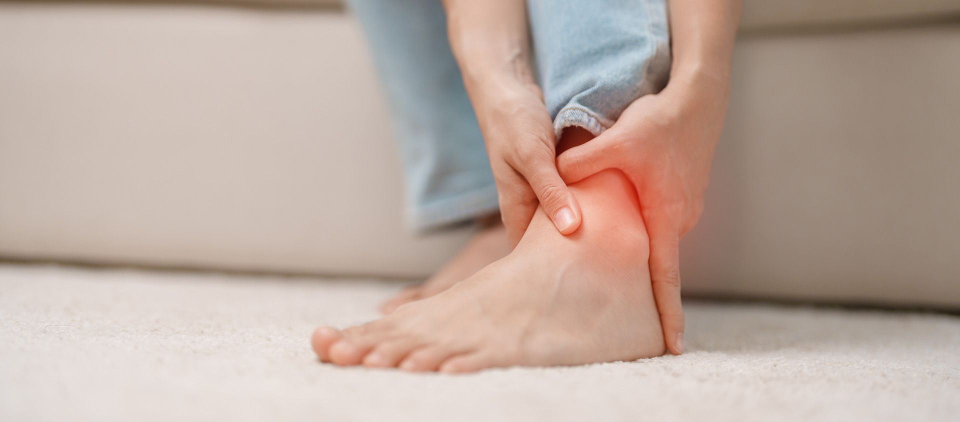 Person holding their ankle, highlighting a red area indicating pain. Sitting indoors.
