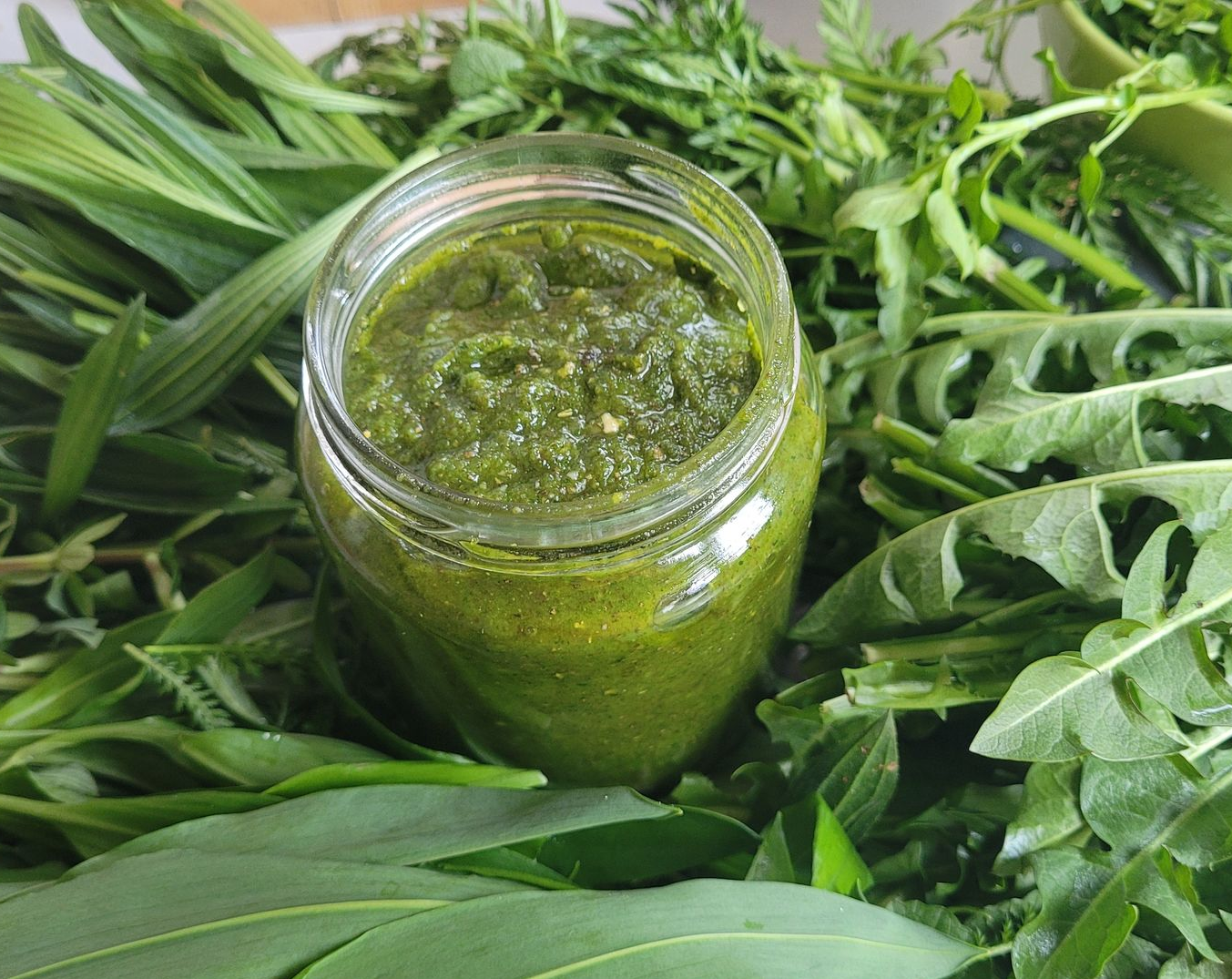 Potje groene kruidensaus omringd door verse groene bladeren