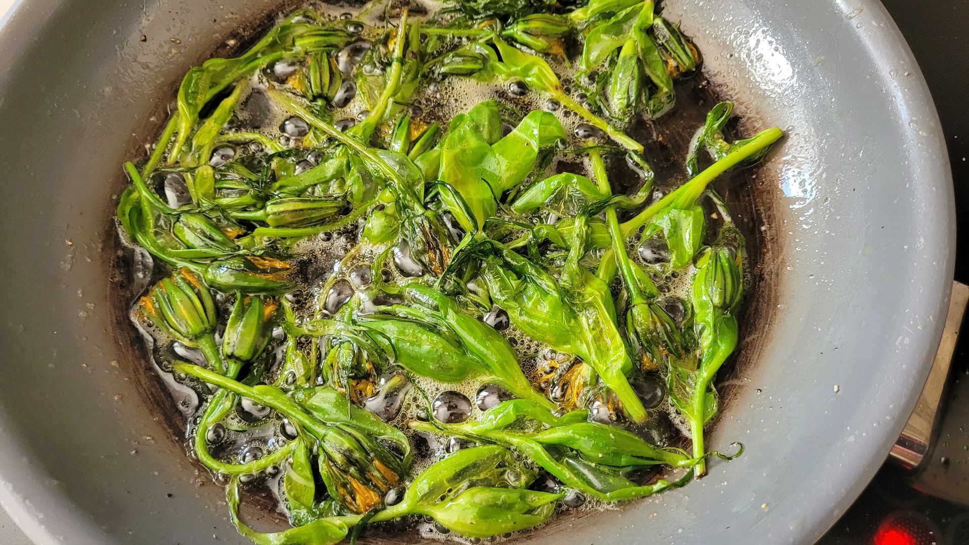 Groene paprika's sissen in olie in een koekenpan, met aangebrande plekjes en borrelende saus.