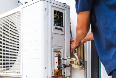 Technician repairing outdoor air conditioning unit; hands working on wires and pipes.