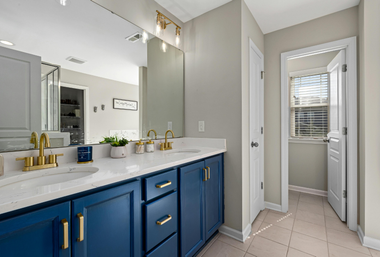 Blue vanity bathroom with gold accents. Open doorway leads to a window with blinds.