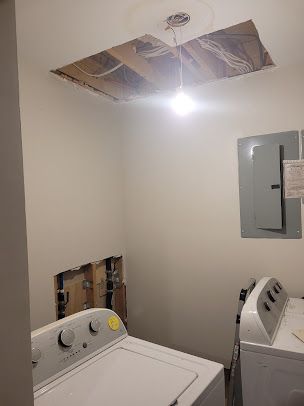 A laundry room with a washer and dryer and a hole in the ceiling.