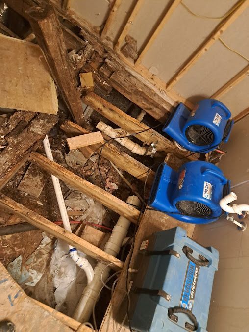 A room with a lot of junk and two blue fans on the floor.