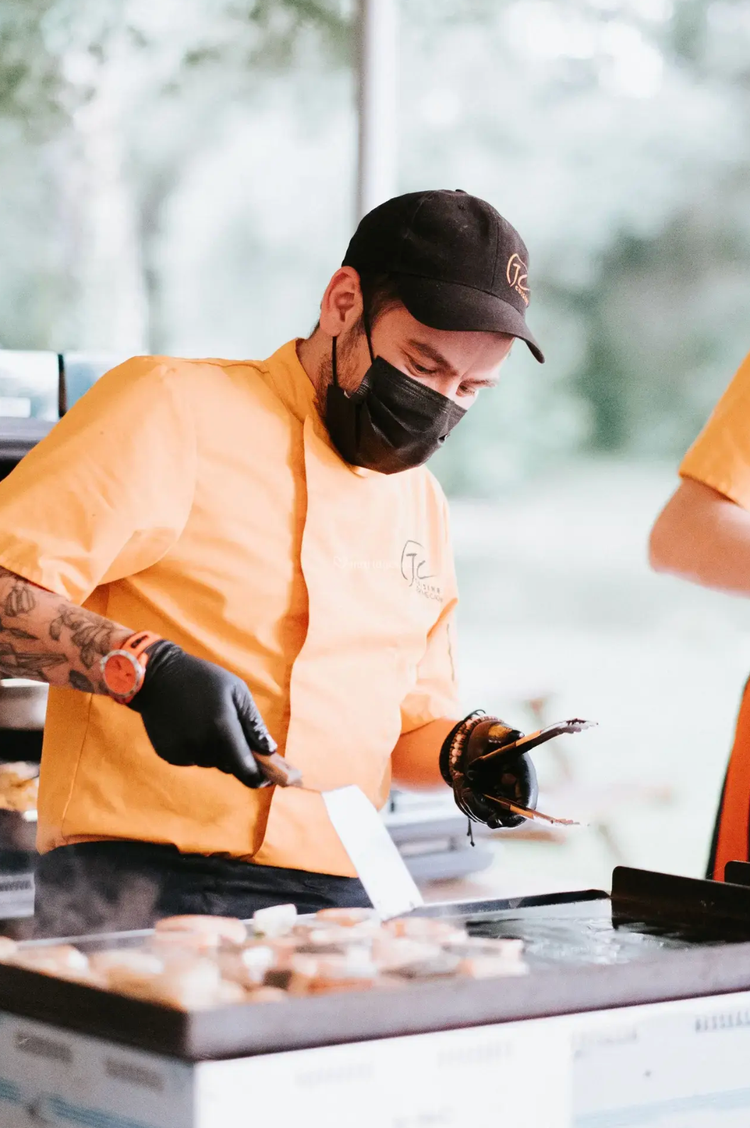 Un homme portant un masque et des gants fait cuire des aliments sur un gril.