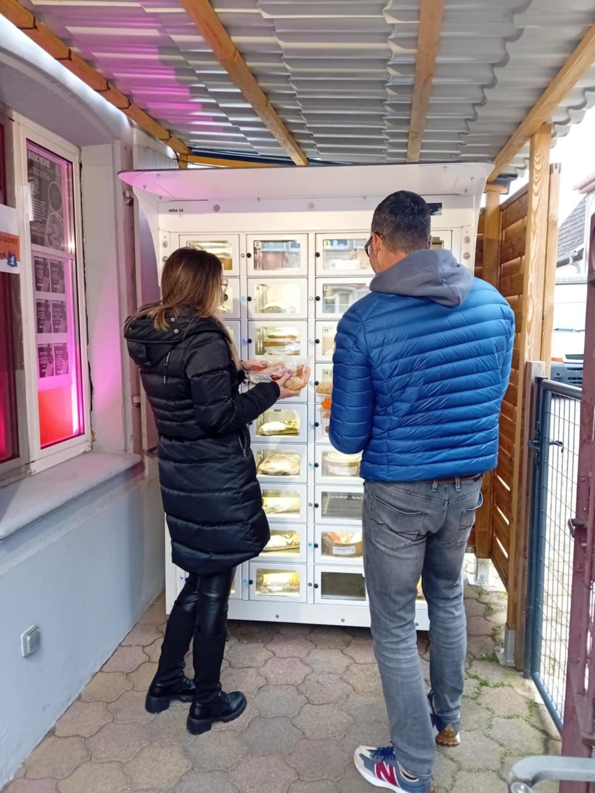 Un homme et une femme se tiennent devant un distributeur automatique.