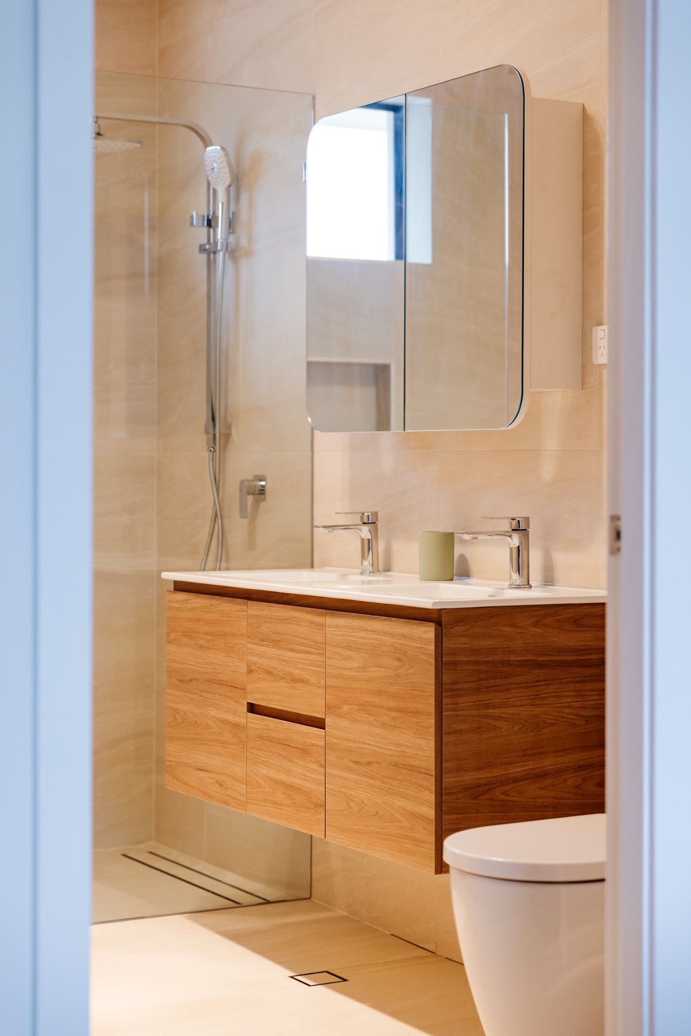 A modern bathroom featuring a floating wooden vanity with dual sinks, a sleek mirror cabinet, and a glass-enclosed shower.